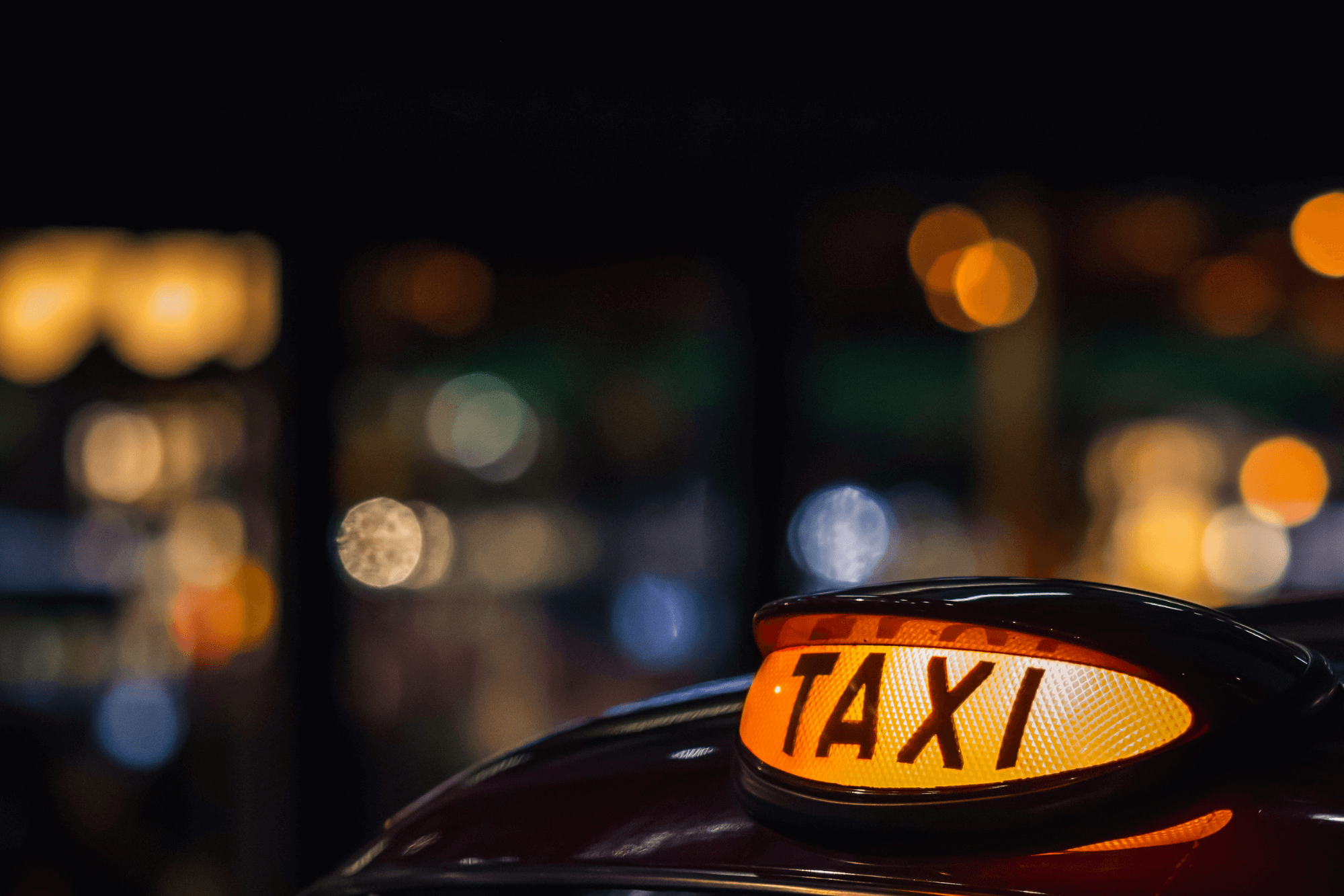 Illuminated taxi sign at night with blurred city lights in the background, representing taxi insurance or private hire cover.