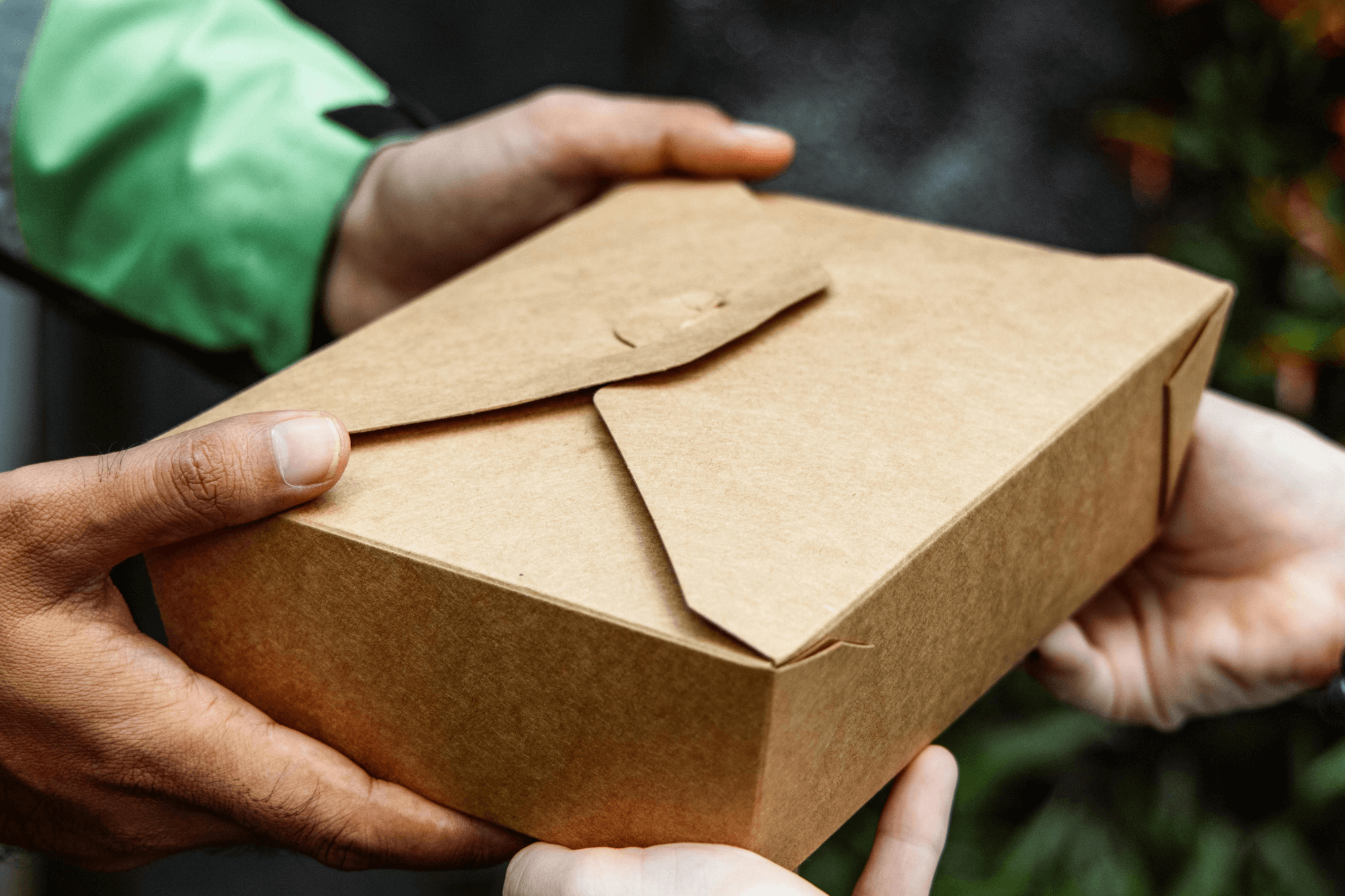 Close-up of a delivery person handing over a brown takeaway box, symbolising courier or delivery driver insurance.