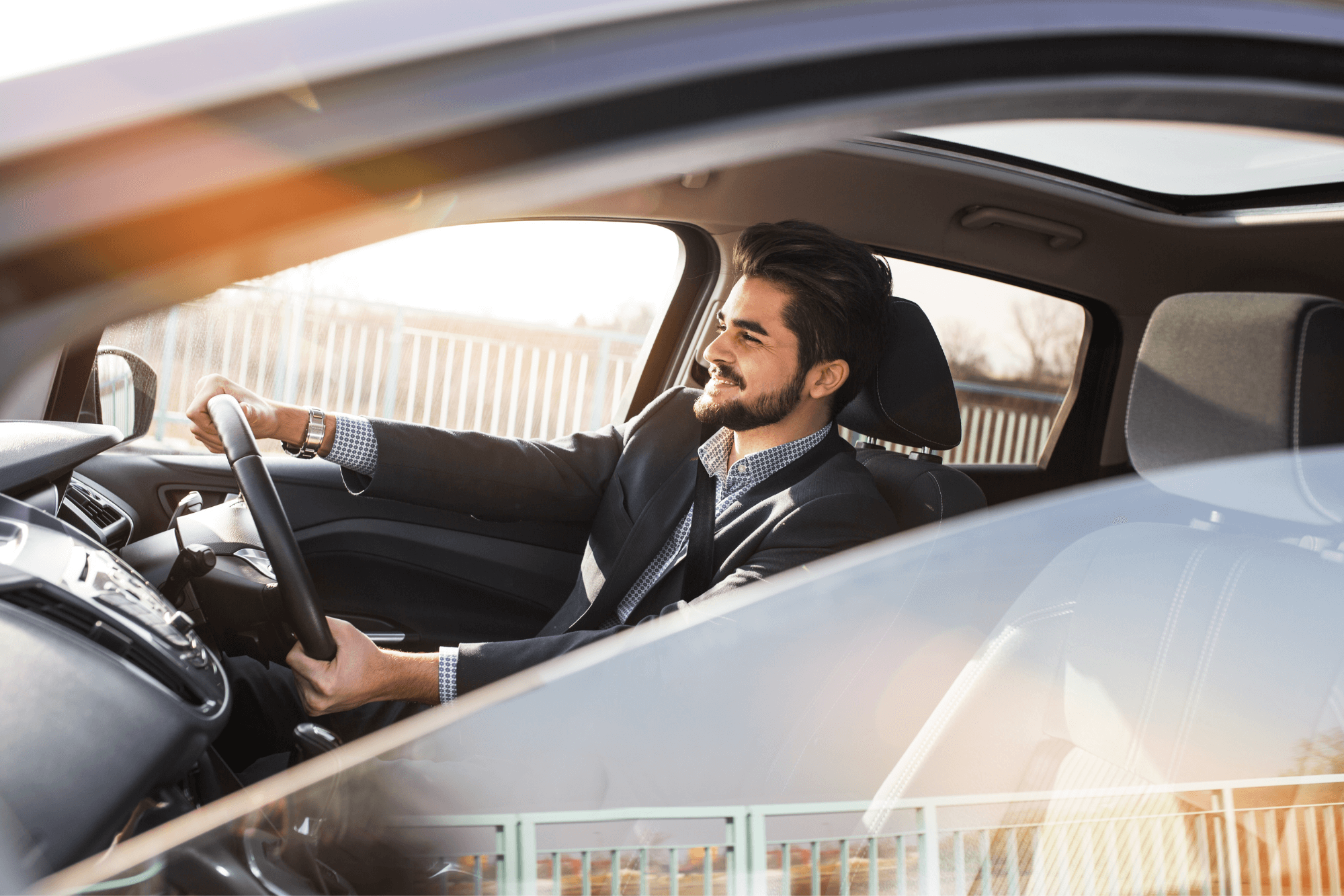 Businessman smiling while driving car during the day, representing professional driver insurance.
