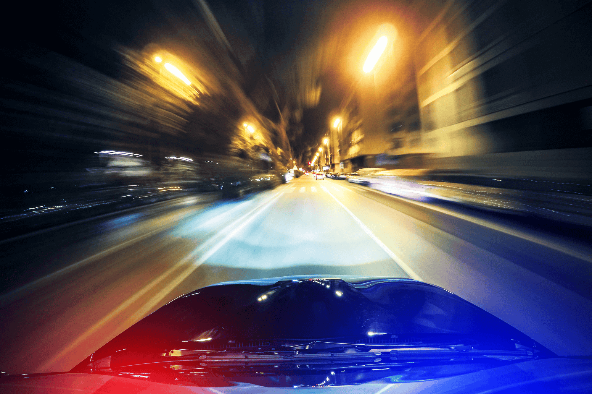 Blurred night road from a moving vehicle’s perspective with police lights, representing speeding or convicted driver insurance.