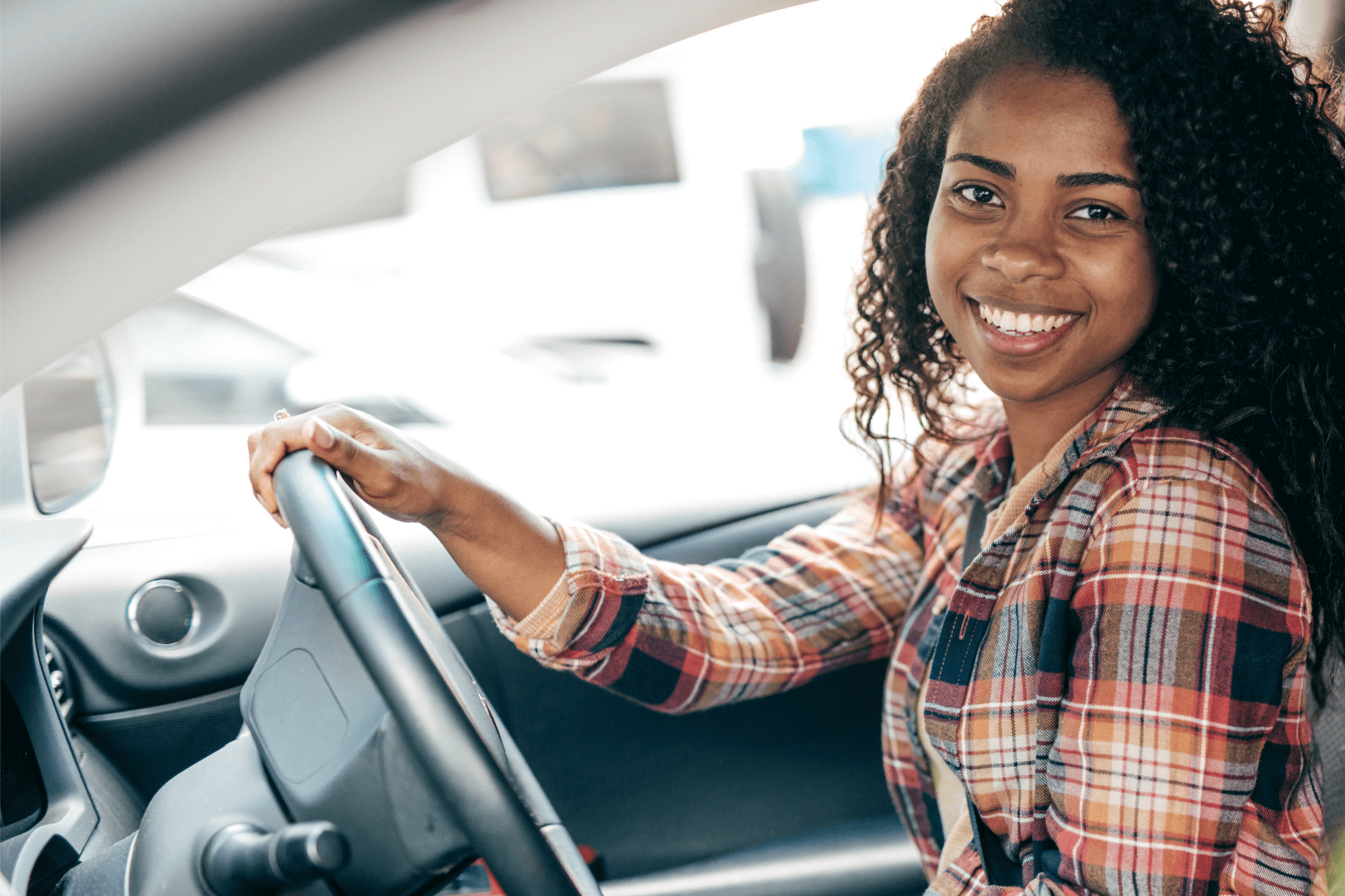 Smiling woman sitting in driver’s seat of her car, representing a young driver new passed.