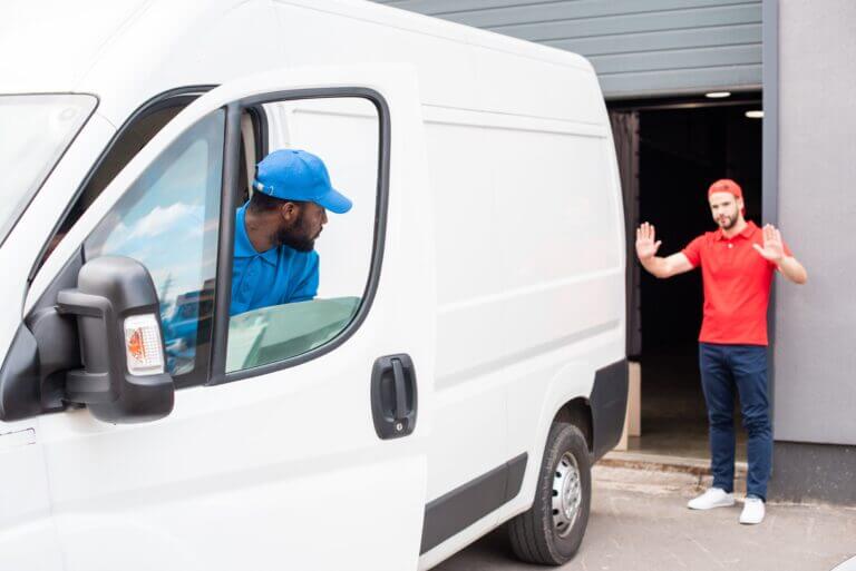 Delivery driver reversing a white van with a colleague guiding him outside a warehouse