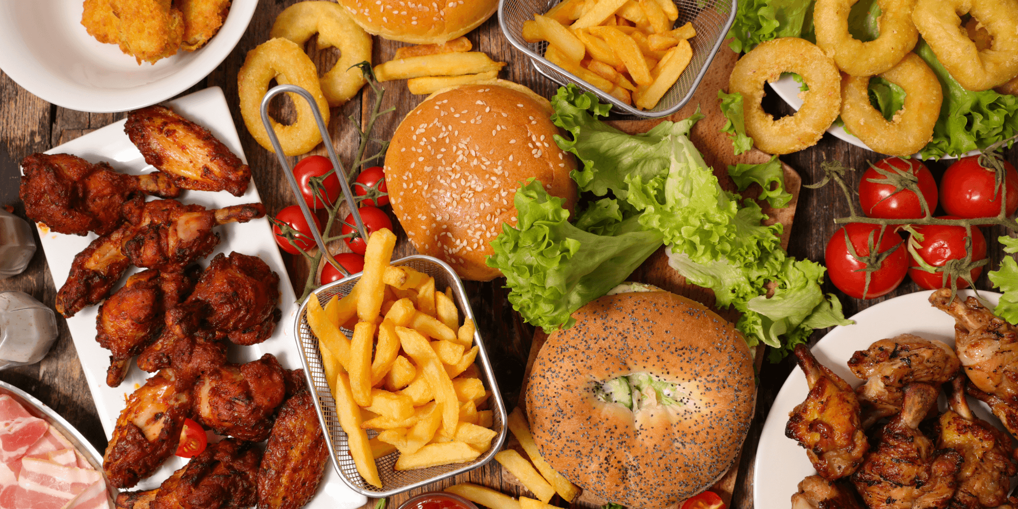 Overhead view of burgers, French fries, onion rings and chicken wings arranged on a rustic table