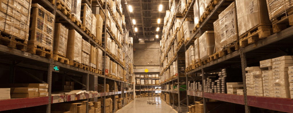 Large warehouse interior with stacked pallets and packaged goods on tall shelves, illustrating the importance of Warehouse Insurance for stock protection.