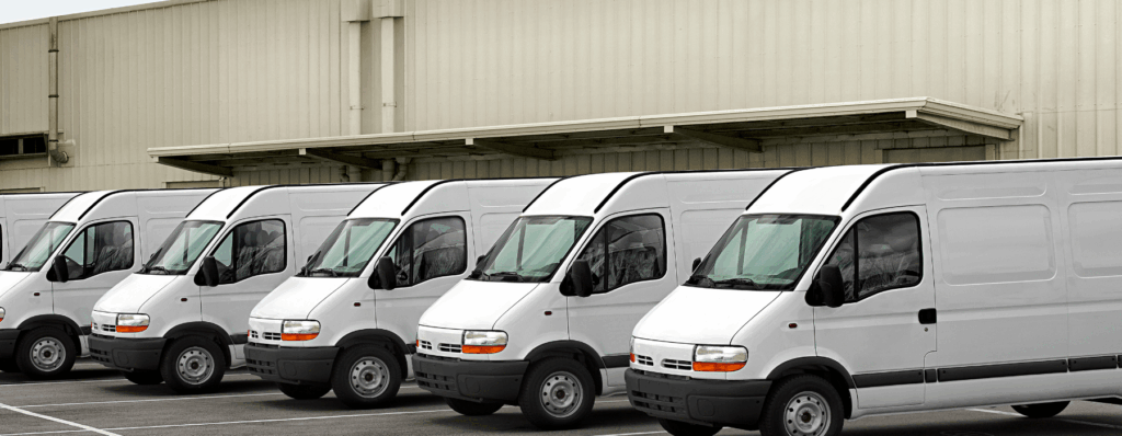 Line of white minibuses parked outside a warehouse, ideal for operators looking for Mini Bus Fleet Insurance to protect multiple vehicles.