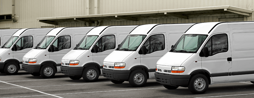Row of white fleet vans parked outside a warehouse – ideal for small business fleet van insurance in the UK