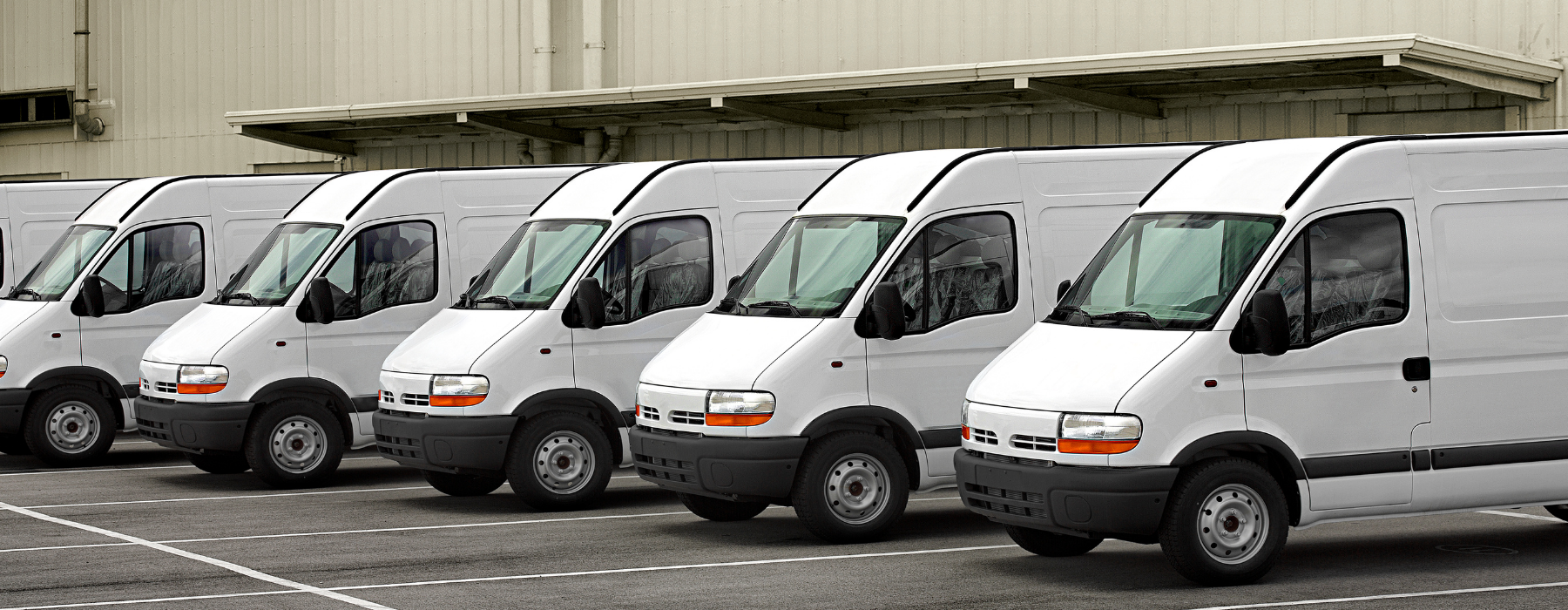 Row of white fleet vans parked outside a warehouse – ideal for small business fleet van insurance in the UK