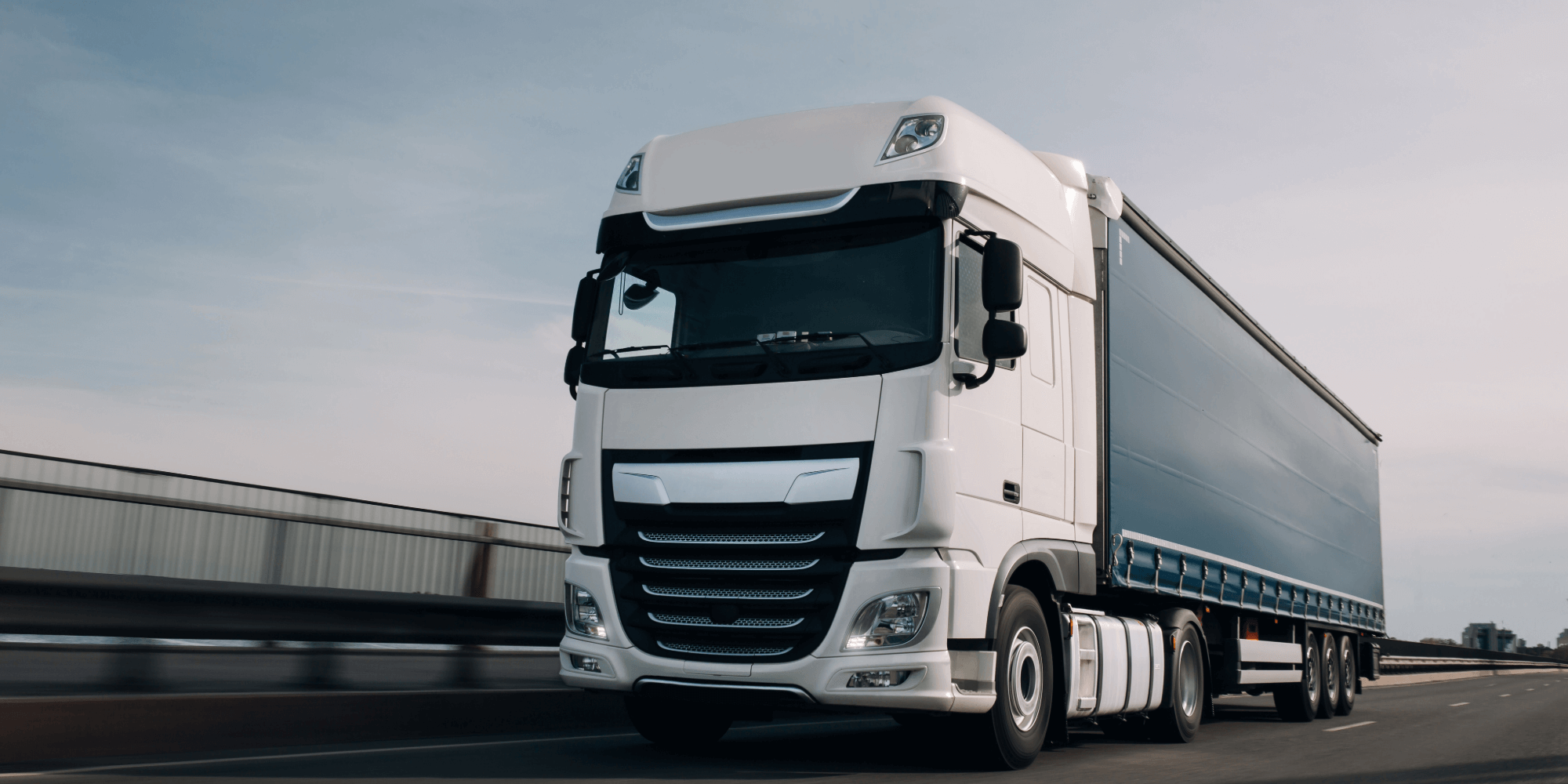 White articulated lorry driving on a motorway during the day.