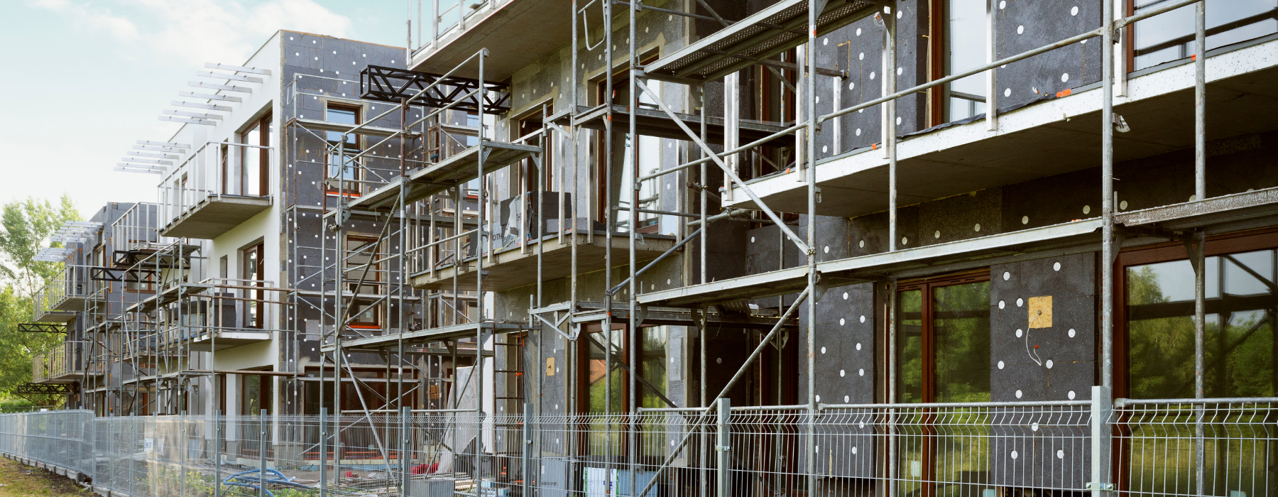A property development site with new apartment buildings under construction, scaffolding in place, and safety fencing around the area.