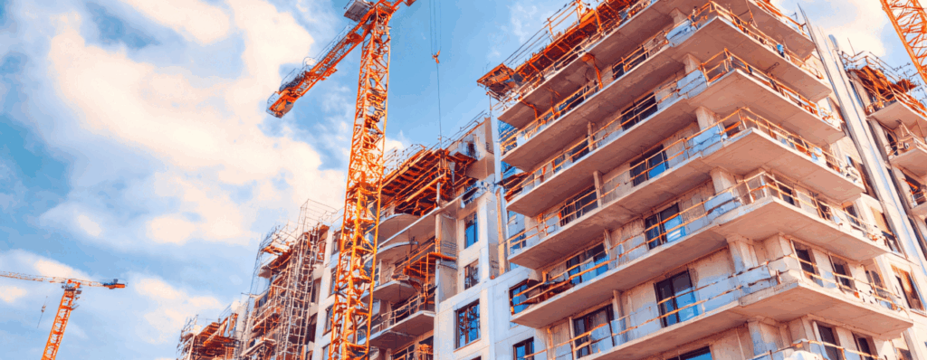 Large residential apartment development under construction with cranes and scaffolding on the exterior, representing the scale and risk involved in property development projects.