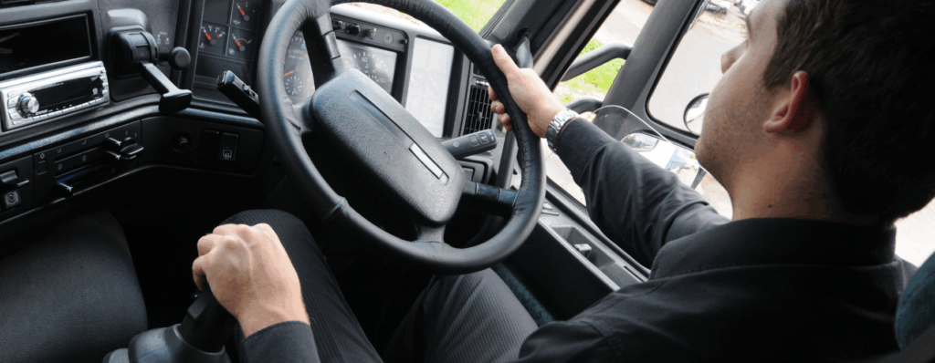 Close-up of an HGV driver holding the steering wheel while driving a large commercial lorry on the road.