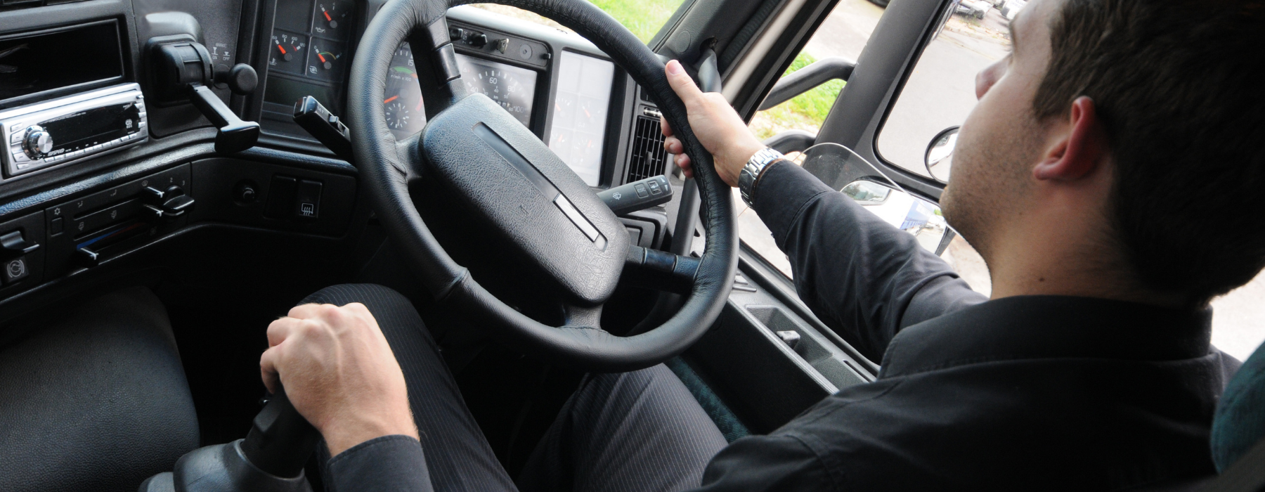 Close-up of an HGV driver holding the steering wheel while driving a large commercial lorry on the road.