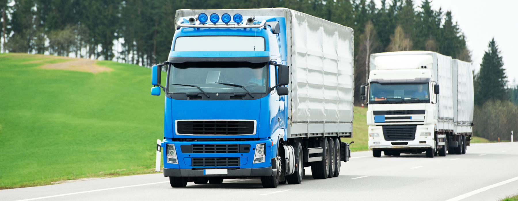 White articulated lorry driving along a UK motorway beneath a gantry sign on a clear day.