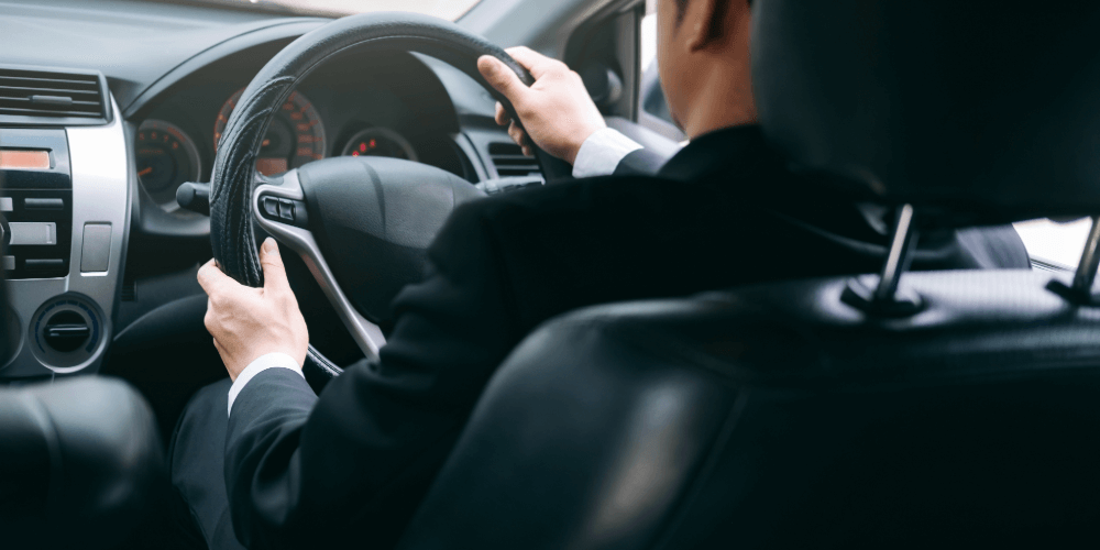 Businessperson driving a car with both hands on the steering wheel, representing safe and focused driving.