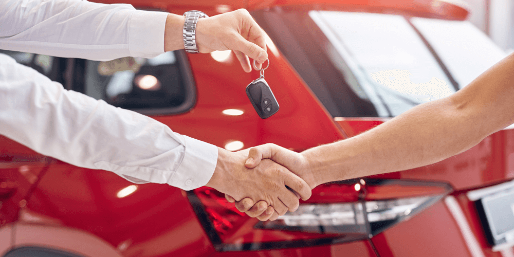 Handshake between two people as car keys are handed over, representing vehicle purchase and insured ownership