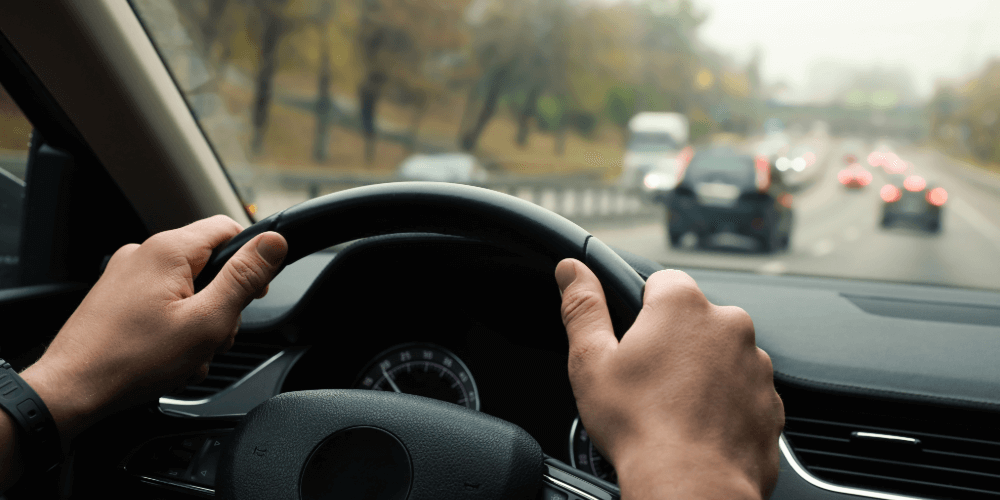 Driver holding the steering wheel while driving in traffic, representing safe and insured driving