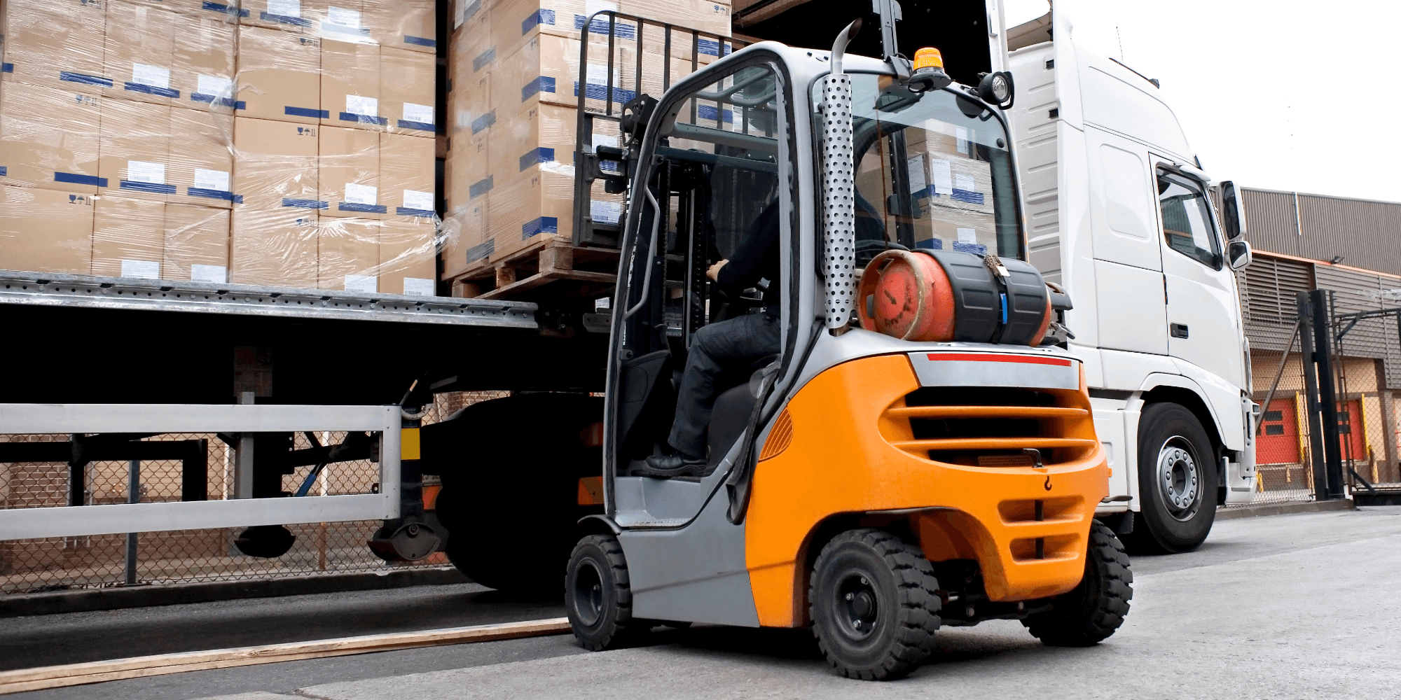 Forklift loading palletised goods into delivery lorry at warehouse loading bay