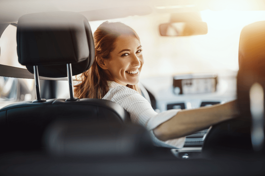 Happy woman driving a car and smiling back, representing reliable personal car insurance