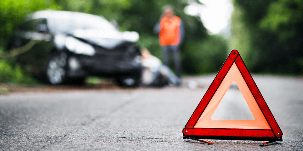 Warning triangle placed on the road after a car accident, with a damaged vehicle in the background
