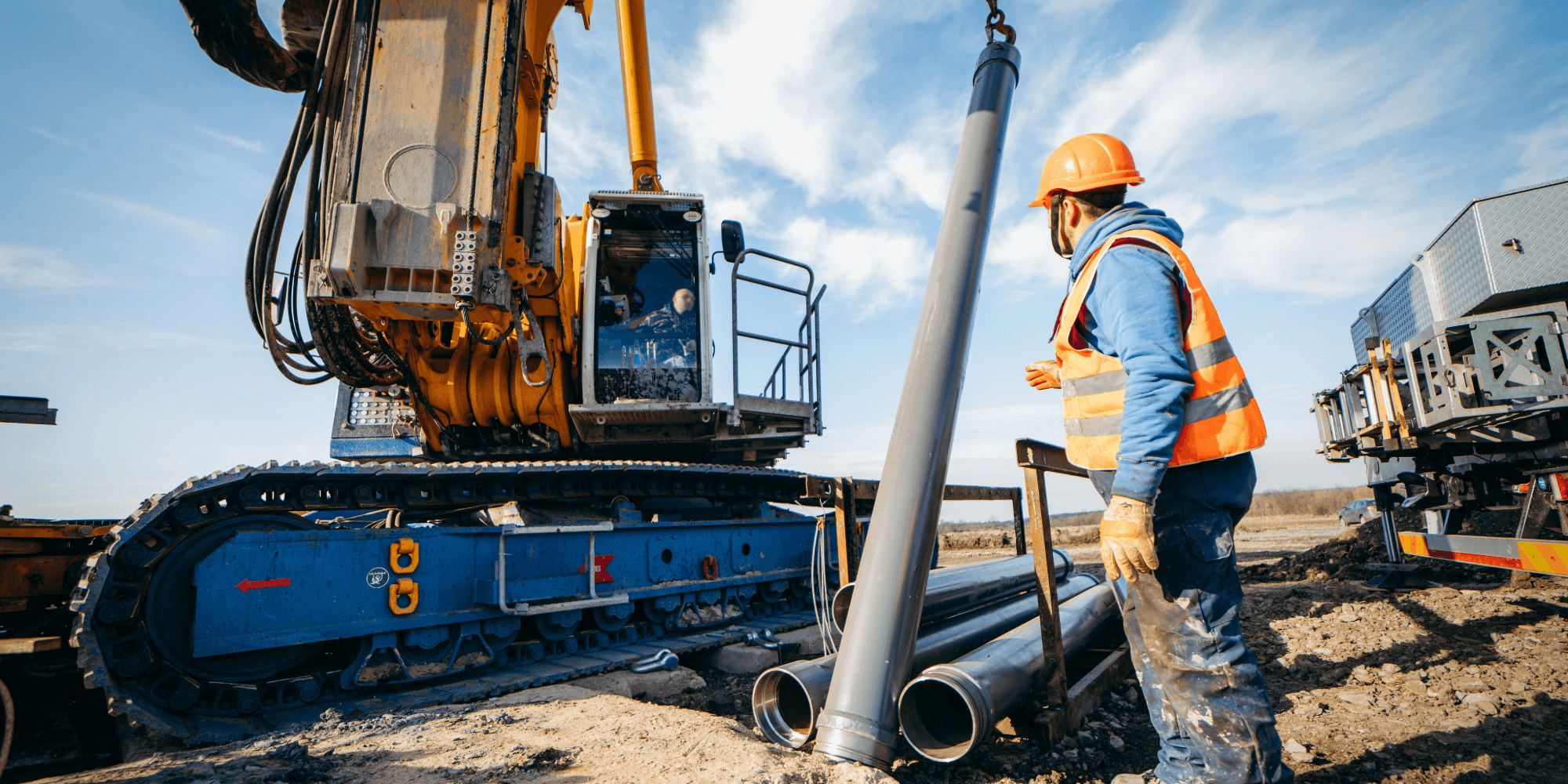 Construction worker guiding heavy machinery while positioning large metal pipes on site