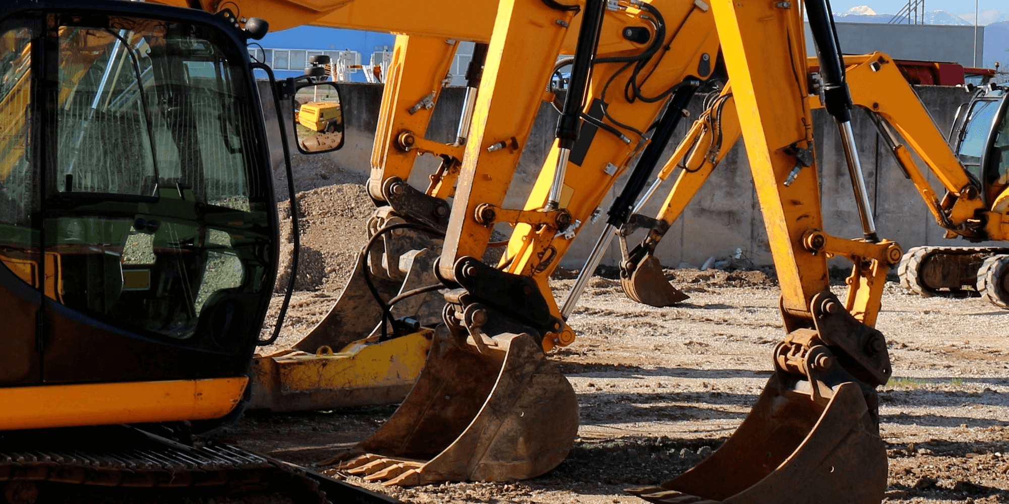 Yellow excavators with buckets resting on the ground at an active construction site